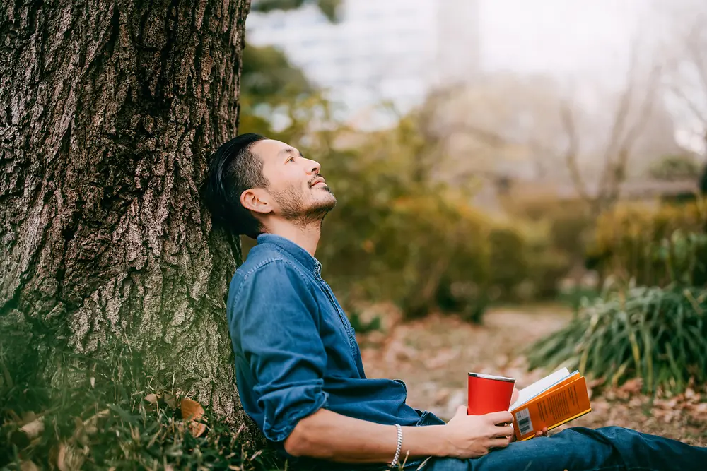 Un homme avec un livre près d’un arbre